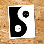 An illustrated risograph print of the yin yang symbol with smiley faces, sits on a wood particle board background.