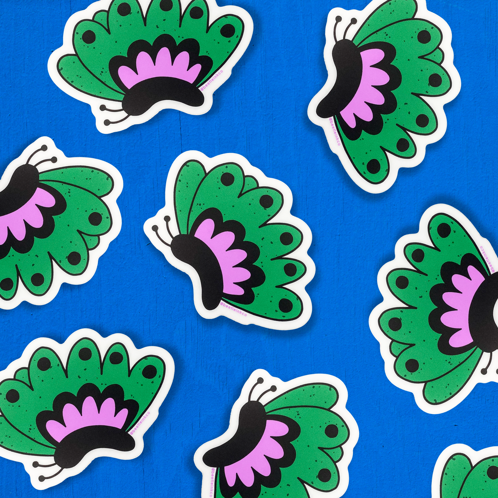 Hand drawn vinyl stickers in the shape of green fluttering butterflies, cover a cobalt blue table.